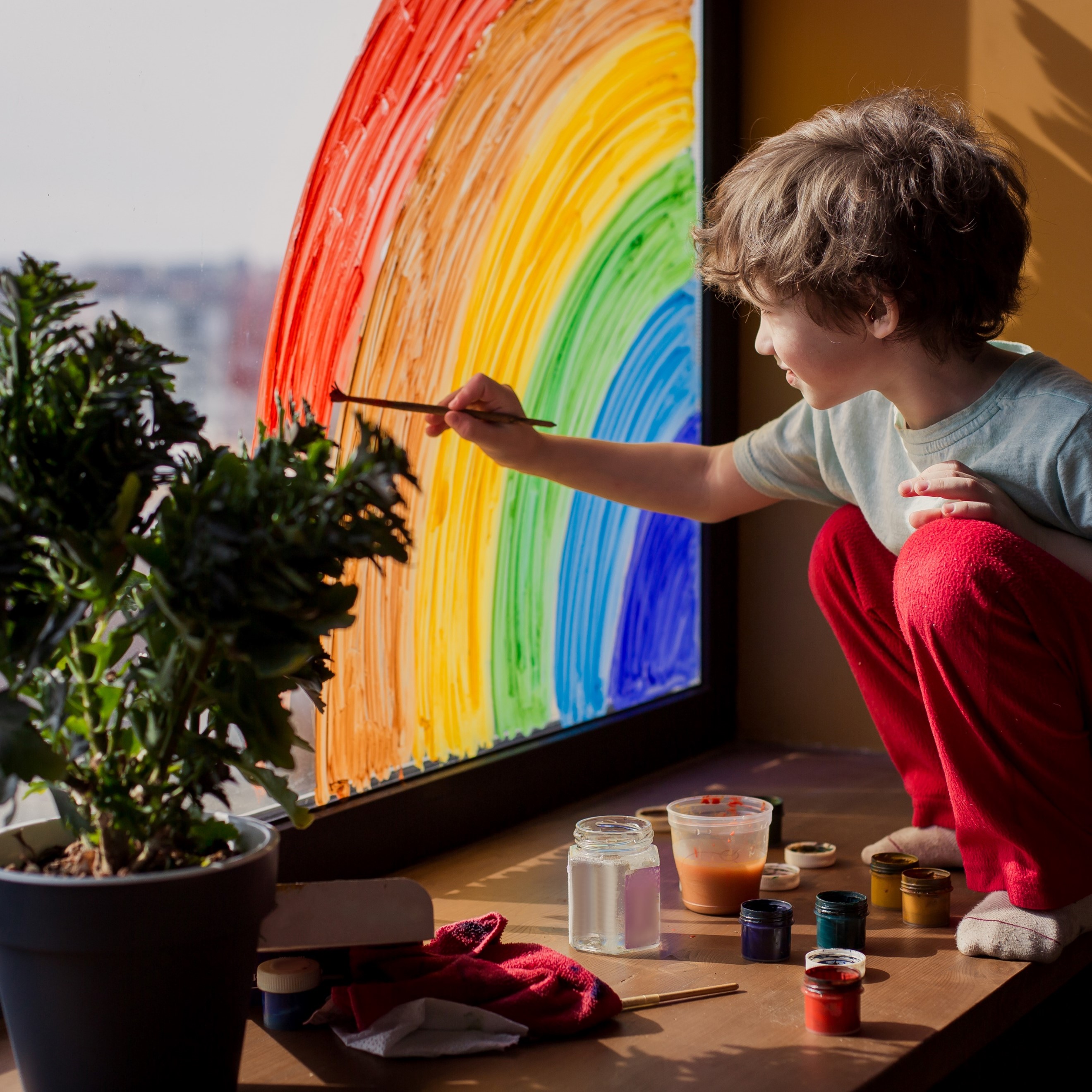 A boy paints a rainbow on a window