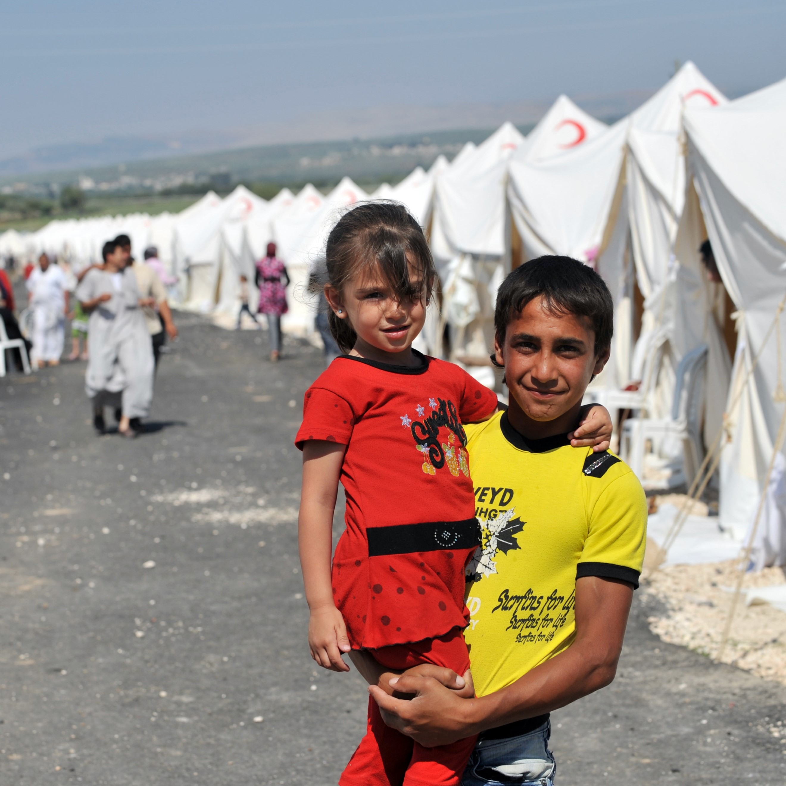 A boy holds a little girl in a refugee camp