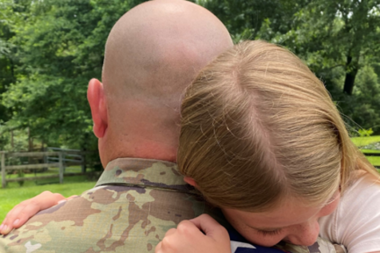Military member hugging a girl holding a flag