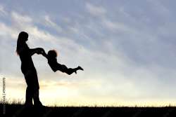 Silhouette image of an adult swinging a child around in the sunset.